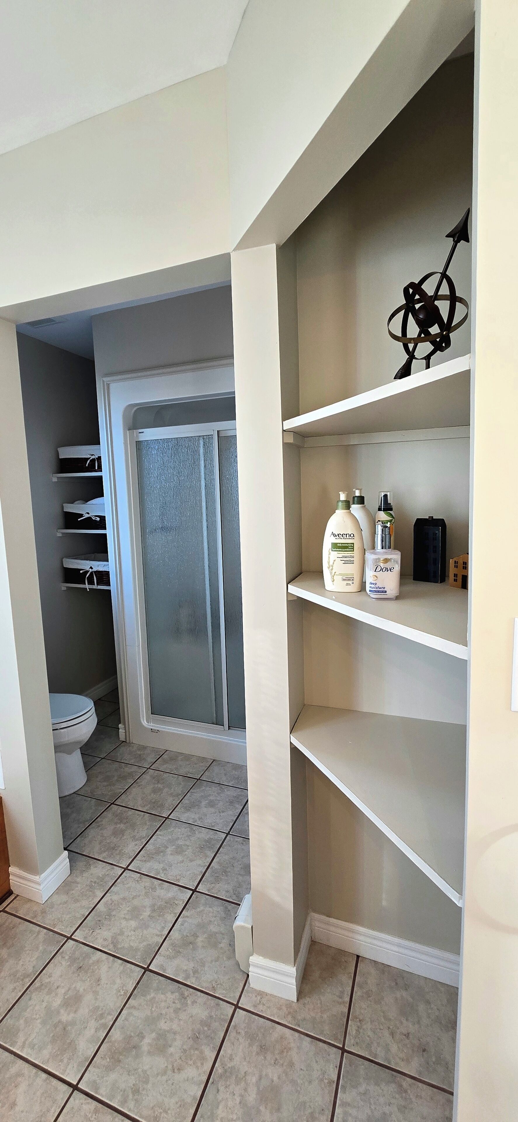 Baño con inodoro, cabina de ducha y tocador con estantes.