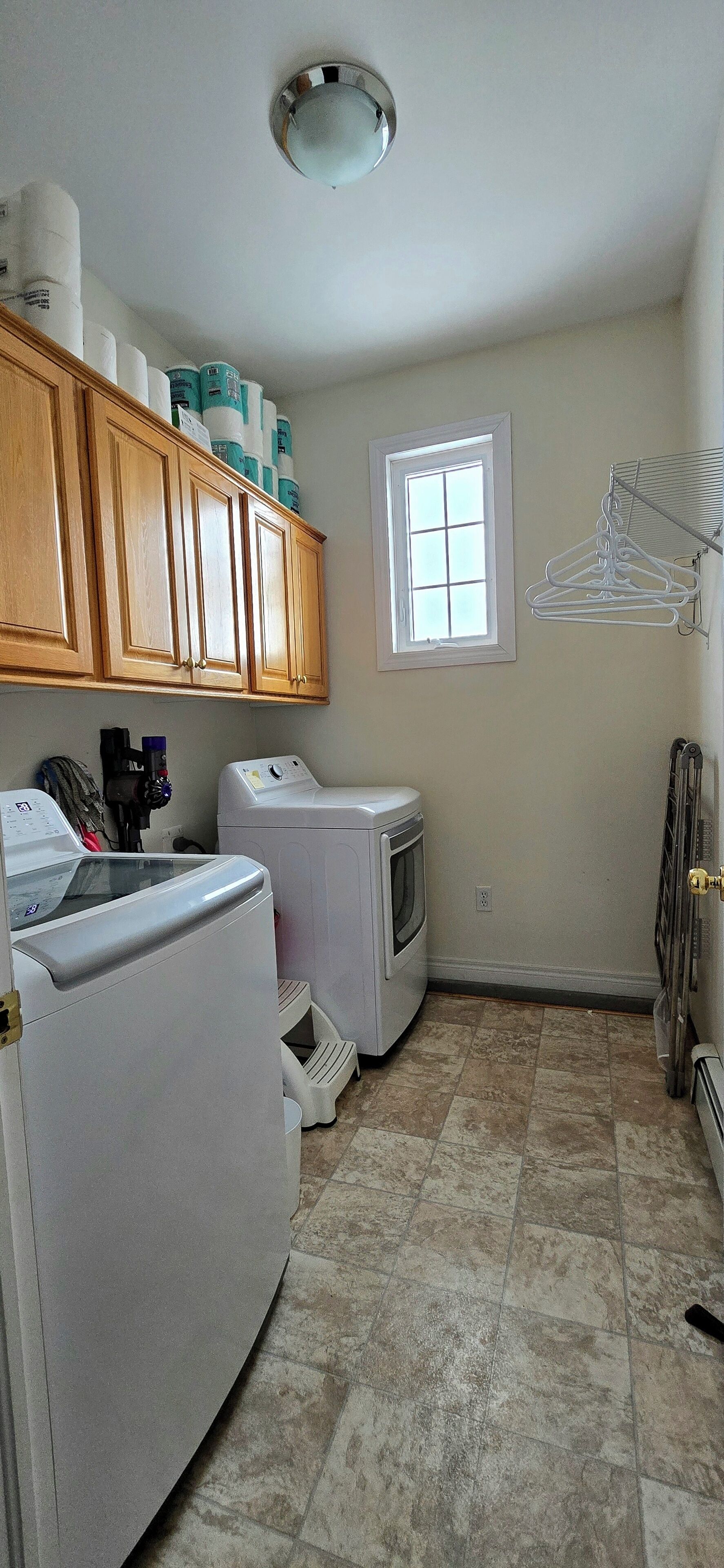 A laundry room with a washing machine, dryer, wooden cabinets, and a window.