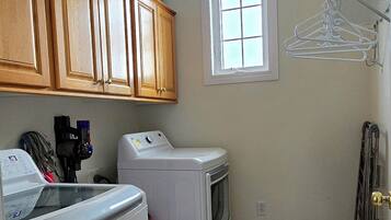 A laundry room with a washing machine, dryer, wooden cabinets, and a window.