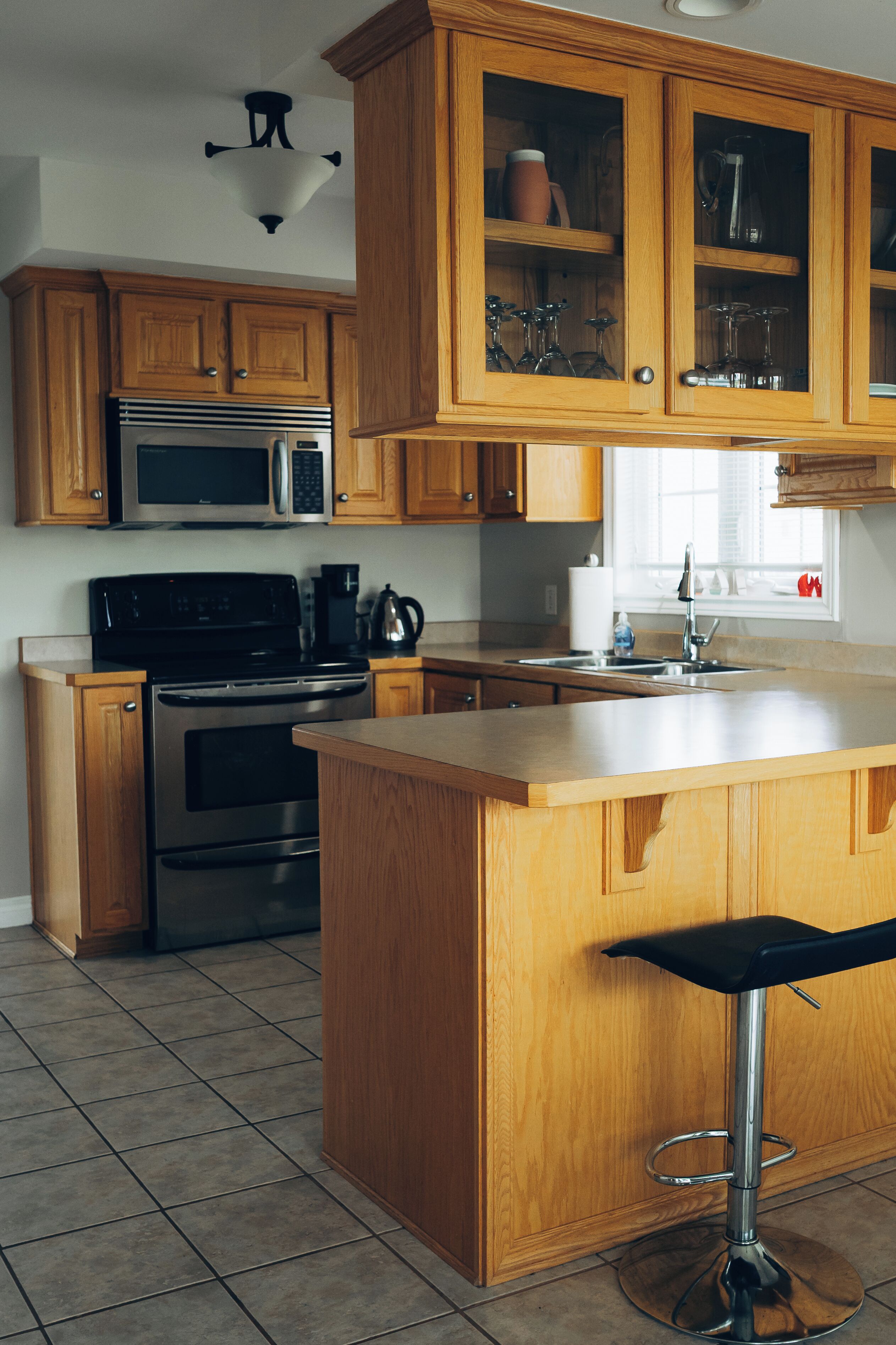 Una cocina con armarios de madera, electrodomésticos de acero inoxidable y un taburete de bar.