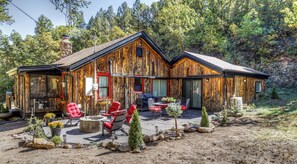 Un chalet rustique doté d’un patio couvert, de meubles d’extérieur et d’une cheminée en pierre.