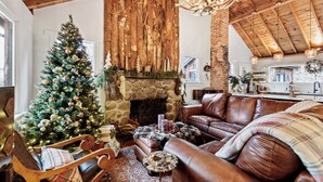 A cozy living room with a Christmas tree, leather sofa, and a stone fireplace. - Cozy river front 3 bedroom Colorado cabin (Colorado Springs)