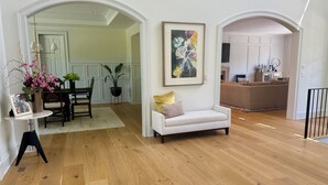 Un vaste espace de vie doté d’un plancher en bois, d’un canapé blanc, d’une table à manger avec des chaises, et d’une cuisine en arrière-plan.