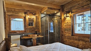 Une chambre de style cabane en bois, avec un lit, une coiffeuse avec un miroir, une douche et une fenêtre donnant sur un immeuble.