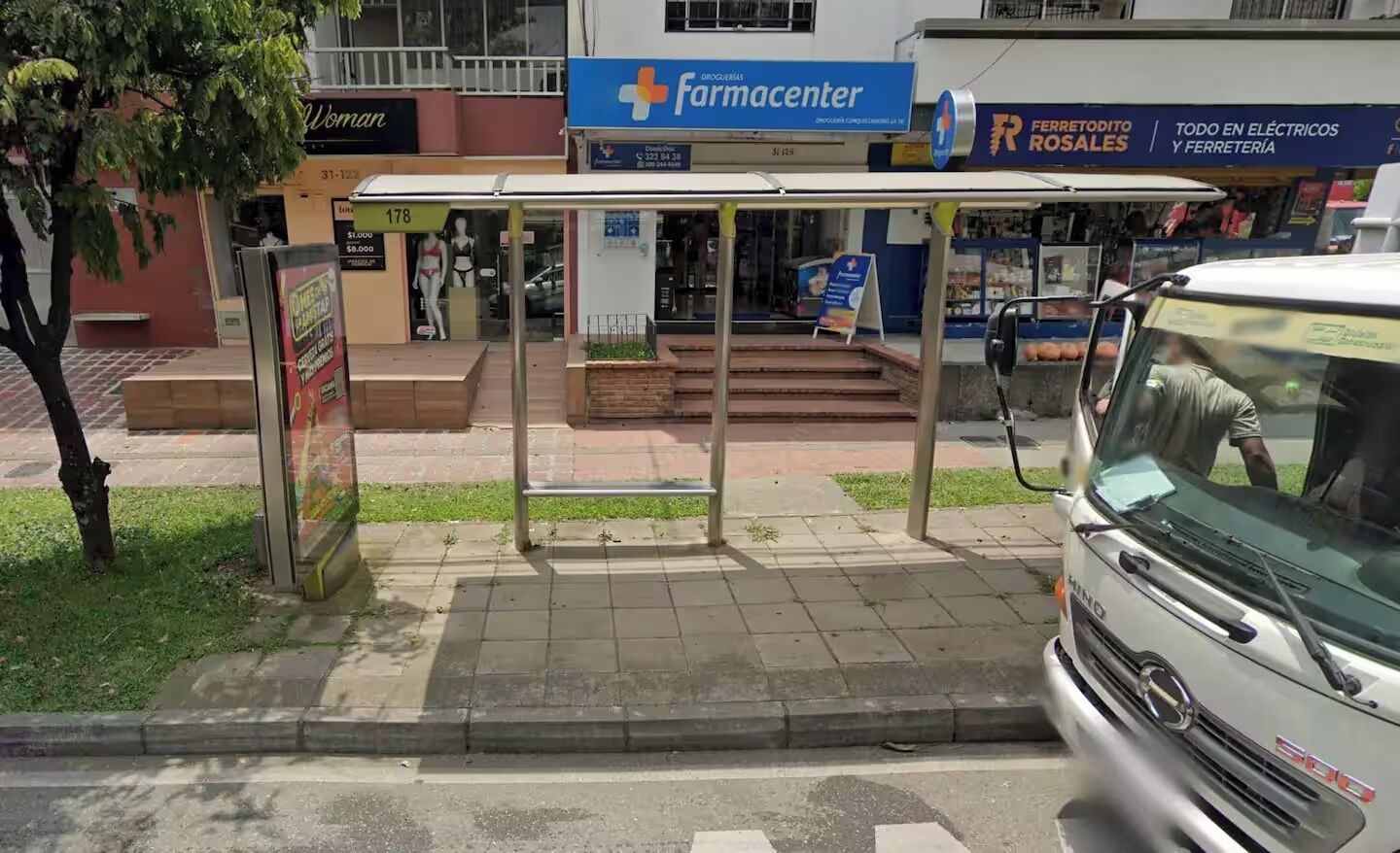 A bus stop with a shelter, a pharmacy, and a bus in motion.