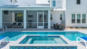 Ein Schwimmbecken mit gefliestem Deck, einer überdachten Terrasse und einem weißen Gebäude mit mehreren Fenstern.