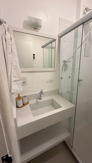 Een moderne badkamer met een wit wastafelmeubel, een spiegel, een handdoek en een douchecabine van glas.