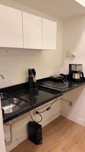 Ett kök med en svart bänkskiva, en diskho i rostfritt stål och en kaffebryggare.