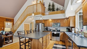 Une cuisine avec des meubles en bois, un îlot central, un escalier et un coin repas comprenant une table et des chaises.