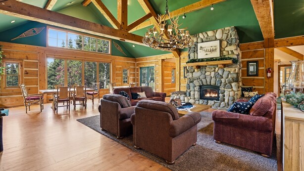 Un intérieur spacieux de chalet en bois, avec une cheminée en pierre, des meubles en bois et de grandes fenêtres.
