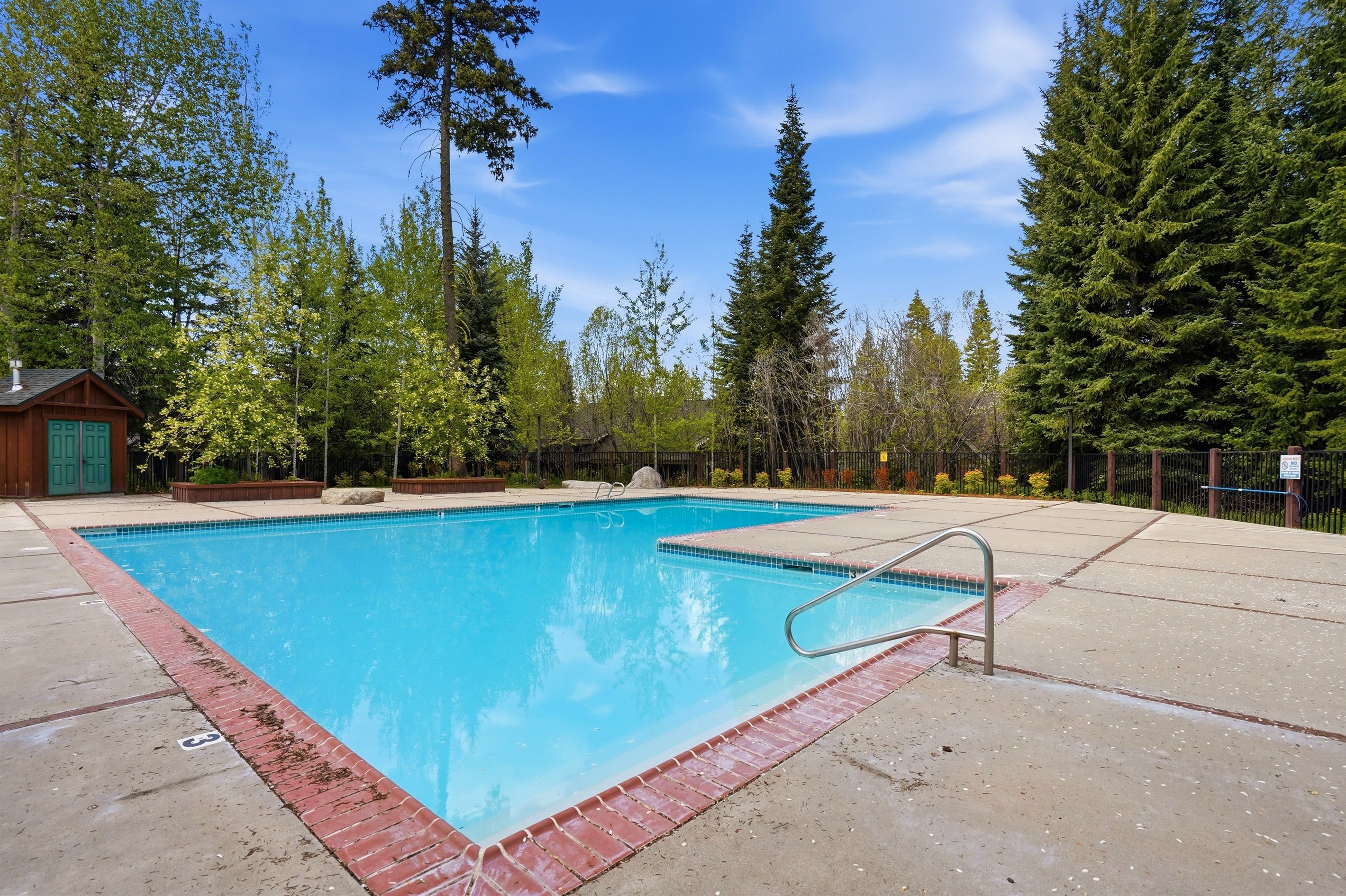A rectangular swimming pool with a red border, surrounded by a concrete deck and a fence.