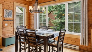 Un intérieur en bois avec une table à manger dressée pour six personnes, de grandes fenêtres et un luminaire suspendu.