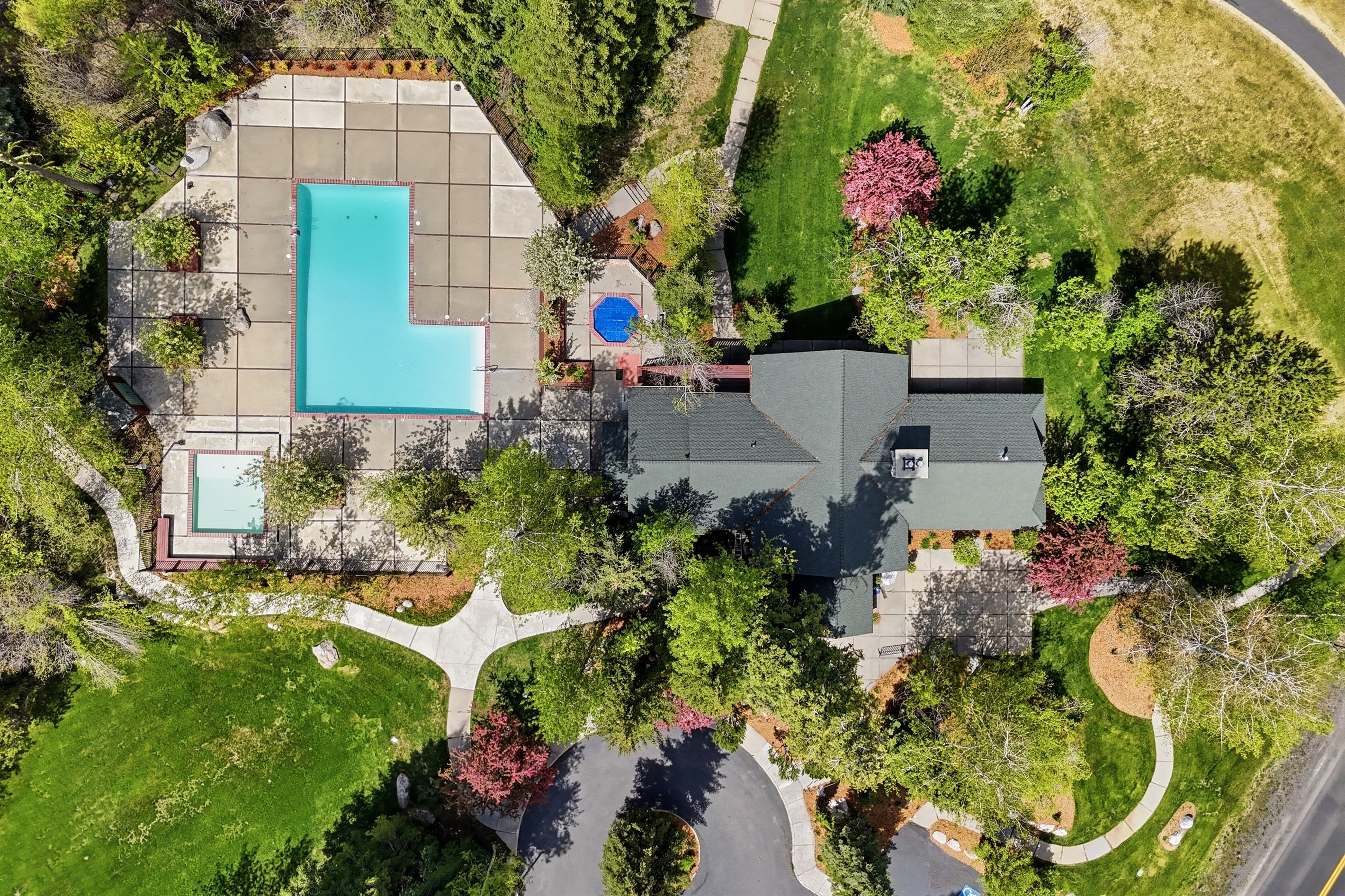An aerial view of a residential property with a swimming pool, a separate hot tub, and a well-maintained lawn.