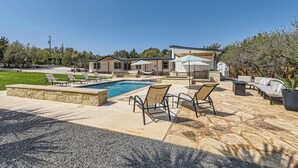 A backyard with a swimming pool, lounge chairs, and a barbecue area. - The Palm Hideaway Oasis with Pool + Hot Tub + Fire pit & Outdoor kitchen! (Spicewood)