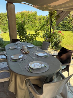 An outdoor dining area with a table set for four, surrounded by chairs, under a canopy.