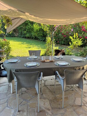 An outdoor dining area with a table set for four, surrounded by stone tiles and under a canopy.