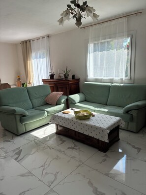 A living room with a green sofa set, a coffee table with a polka dot tablecloth, and a vase with flowers on a wooden side table.