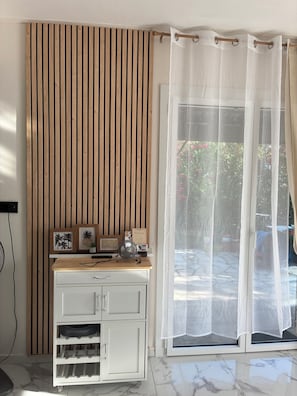 A room with a wooden slat wall, a white cabinet with drawers, a small fan, and a window with sheer curtains.