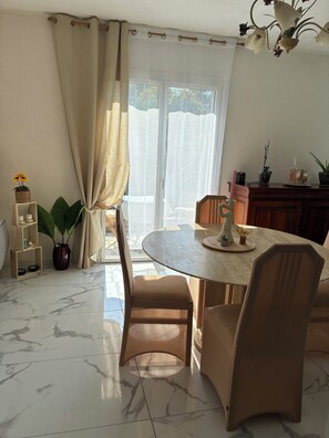 A dining area with a round table, chairs, a potted plant, and a window with curtains.