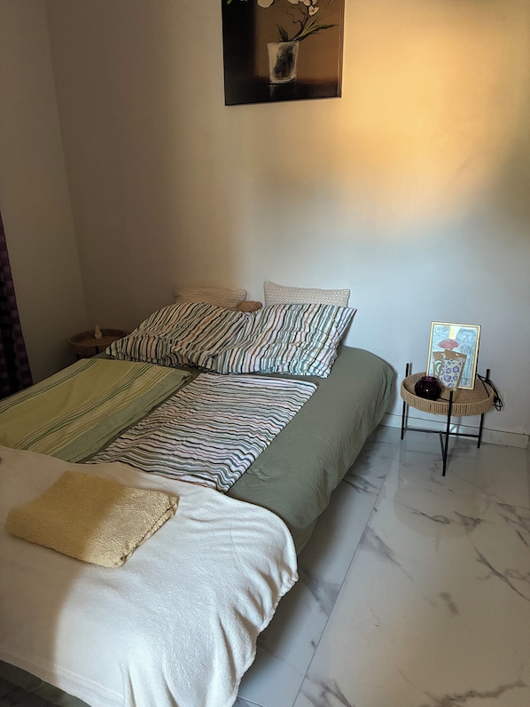 A neatly made bed with striped bedding, a small bedside table with a vase and picture frame, and a wall-mounted picture above the bed.