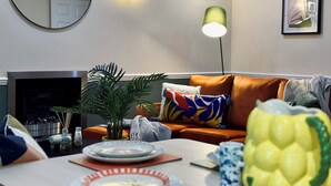 A living room with a sofa, a coffee table, a lamp, and a plant. - Spacious Home | Free Parking | WiFi | Sleeps 8! (Gravesend)