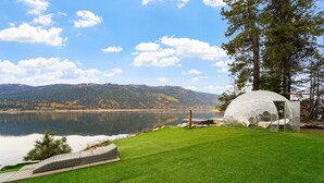 Estrutura em forma de cúpula perto de um lago, com céu claro e montanhas ao fundo.