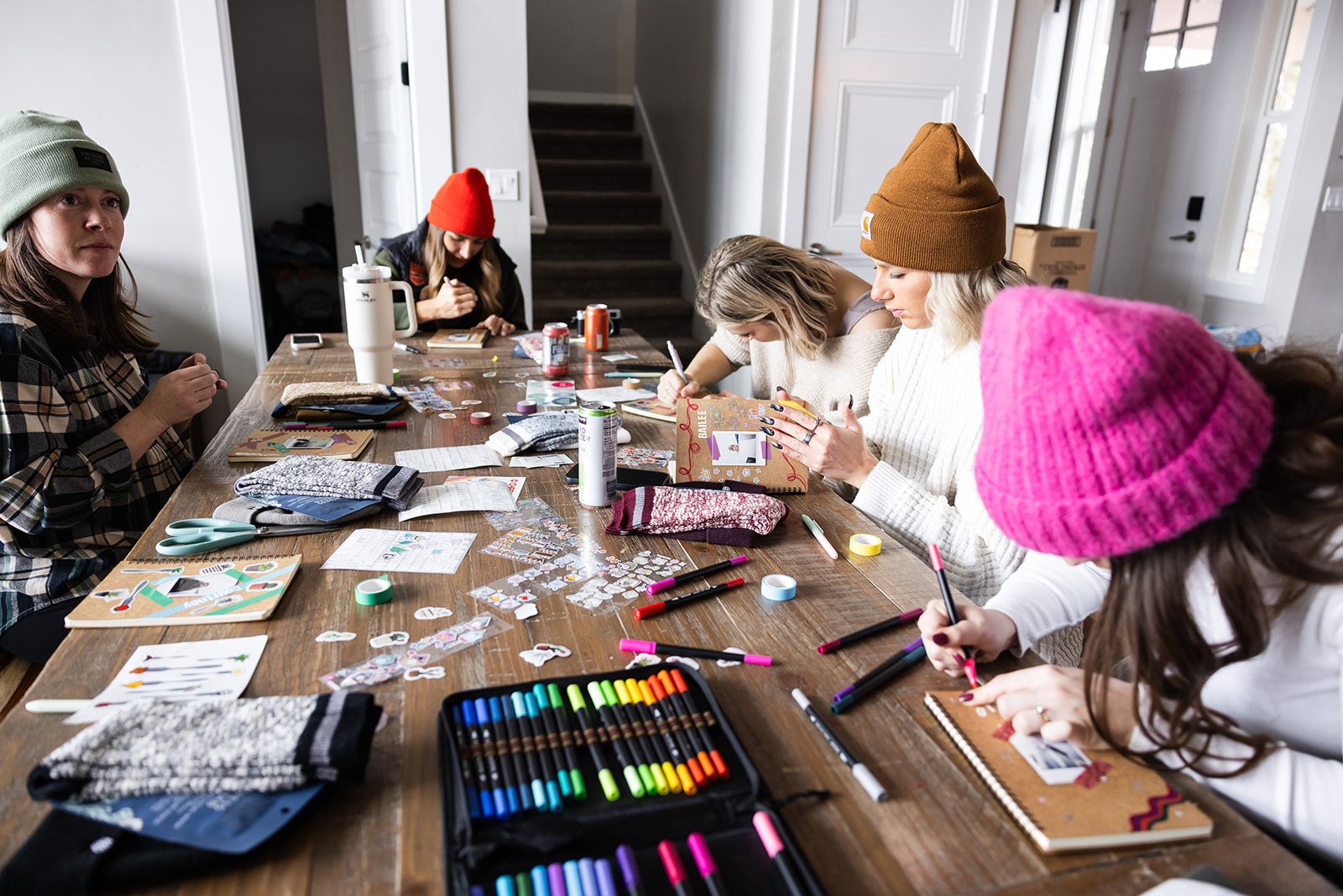 A group of people engaged in a craft activity at a wooden table cluttered with art supplies and materials.