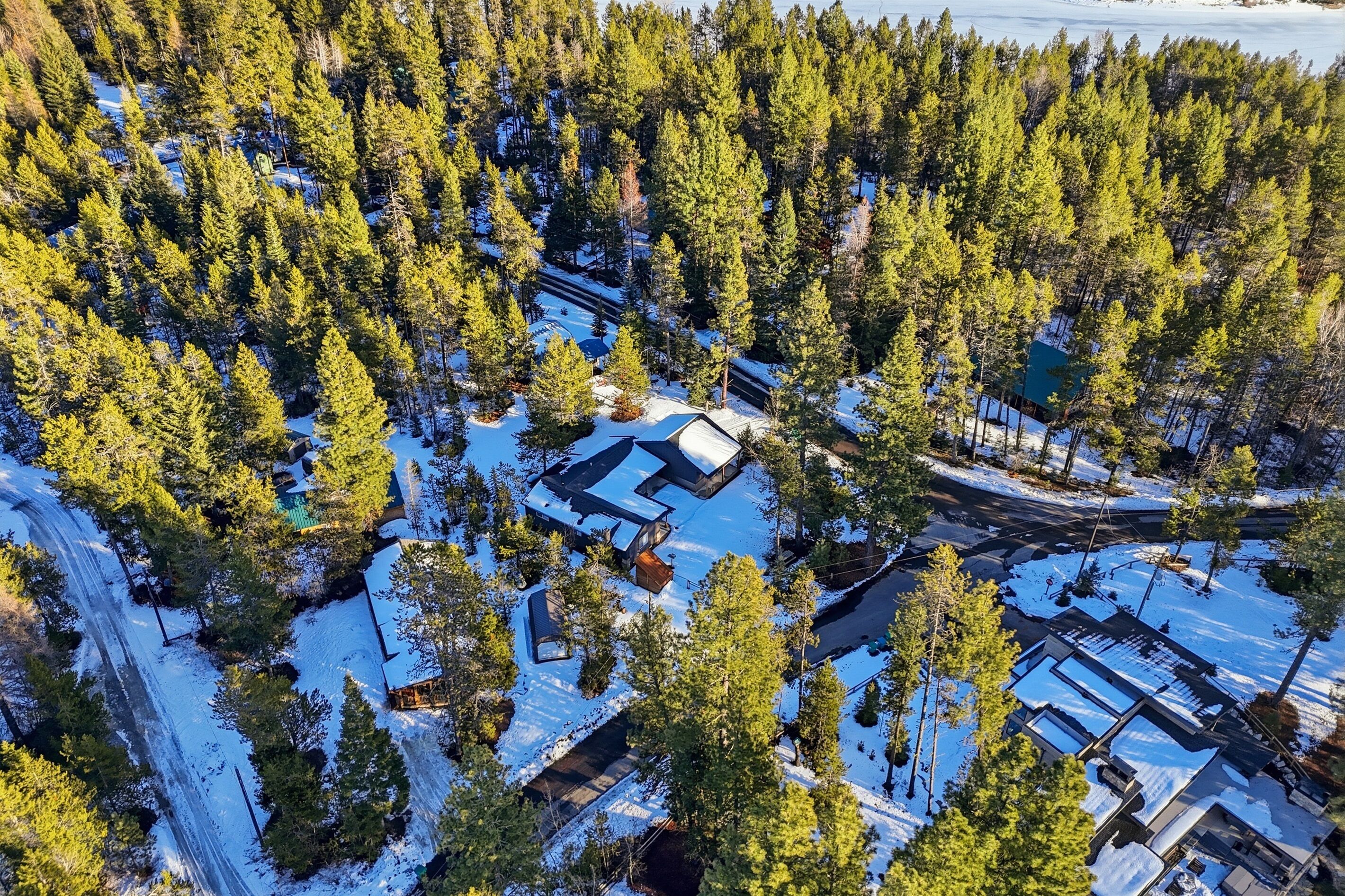 An aerial view of a cabin surrounded by a dense forest with snow-covered ground.