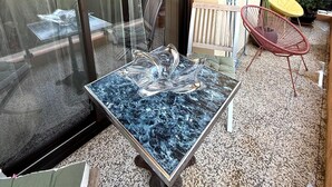 Un balcon avec une porte vitrée, une table en marbre, une chaise rouge et un pot de fleurs.