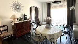 Un coin repas comprenant une table ronde, des chaises, un lustre, une commode et un miroir.
