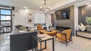 Een moderne woonkamer met een bank, stoelen, een salontafel, een open haard en een aan de muur bevestigde televisie.