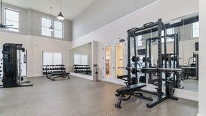 Een ruime fitnessruimte met diverse trainingsapparatuur, grote ramen en een hoge plafond.