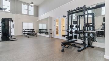 A spacious gym with various exercise equipment, large windows, and a high ceiling.
