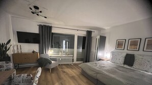 Una camera da letto moderna con un letto, una sedia, una cassettiera, un termosifone e un'ampia finestra con tende.
