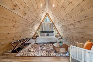 A cozy attic bedroom with a large bed, a round wooden table, and a hanging chair. - Stunning A-Frame w/ Hot Tub + Epic Mountain Views!! 10 mins to Pigeon Forge. (Sevierville)