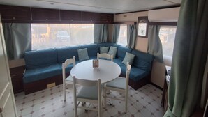 A compact living space with a blue sofa, a round table, and chairs. - MOBIL HOME MARMOTTES 6 PERS (Besse-et-Saint-Anastaise)