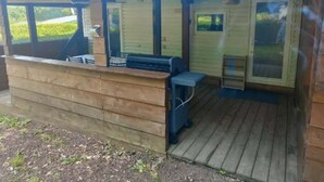 A wooden cabin with a porch, a grill, and a small seating area. - MOBIL HOME MARMOTTES 6 PERS (Besse-et-Saint-Anastaise)
