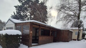 A wooden cabin with a snow-covered roof and a covered porch, surrounded by trees and a snow-covered yard. - MOBIL HOME MARMOTTES 6 PERS (Besse-et-Saint-Anastaise)
