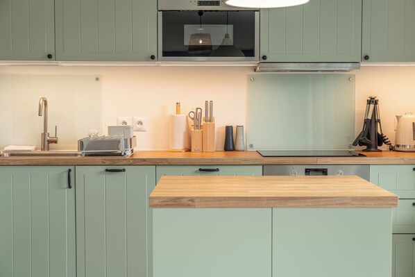 Een moderne keuken met lichtgroene kastjes, een houten aanrechtblad en roestvrijstalen apparatuur.