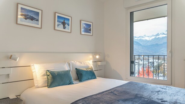 Quarto com uma cama grande, mesa de cabeceira e janela com vista para a montanha.