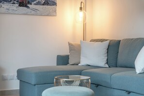 Een moderne woonkamer met een blauwe bank, een glazen salontafel en een vloerlamp.