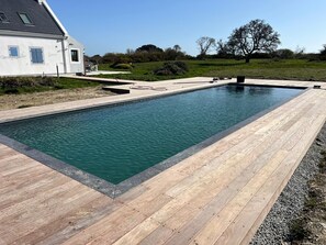 En rektangulär swimmingpool med ett trädäck runt om, placerad på en gräsyta med ett hus i bakgrunden.