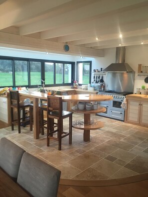 A modern kitchen with a large island, wooden chairs, a built-in oven, and large windows offering a view of the outdoors. - Magnificent house with swimming pool close to the palace (Le Palais)