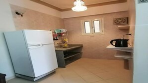 Uma cozinha compacta com geladeira branca, bancada pequena, luminária pendente e janela de dois vidros.