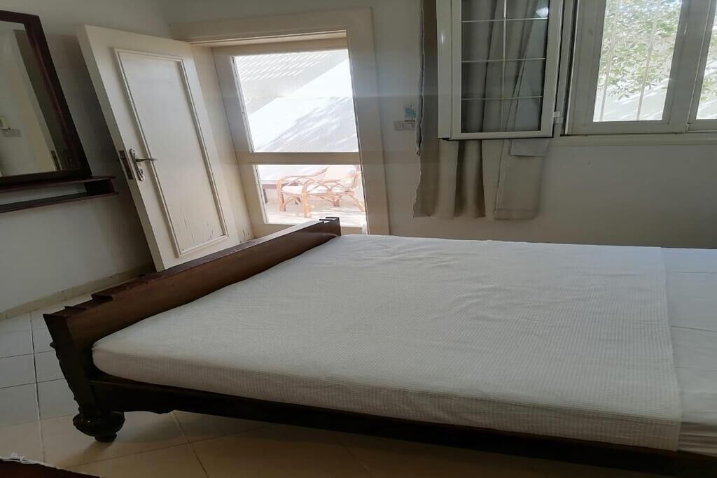 Ein Schlafzimmer mit einem Bett, einer Tür, einem Fenster mit Vorhang und Blick ins Freie.