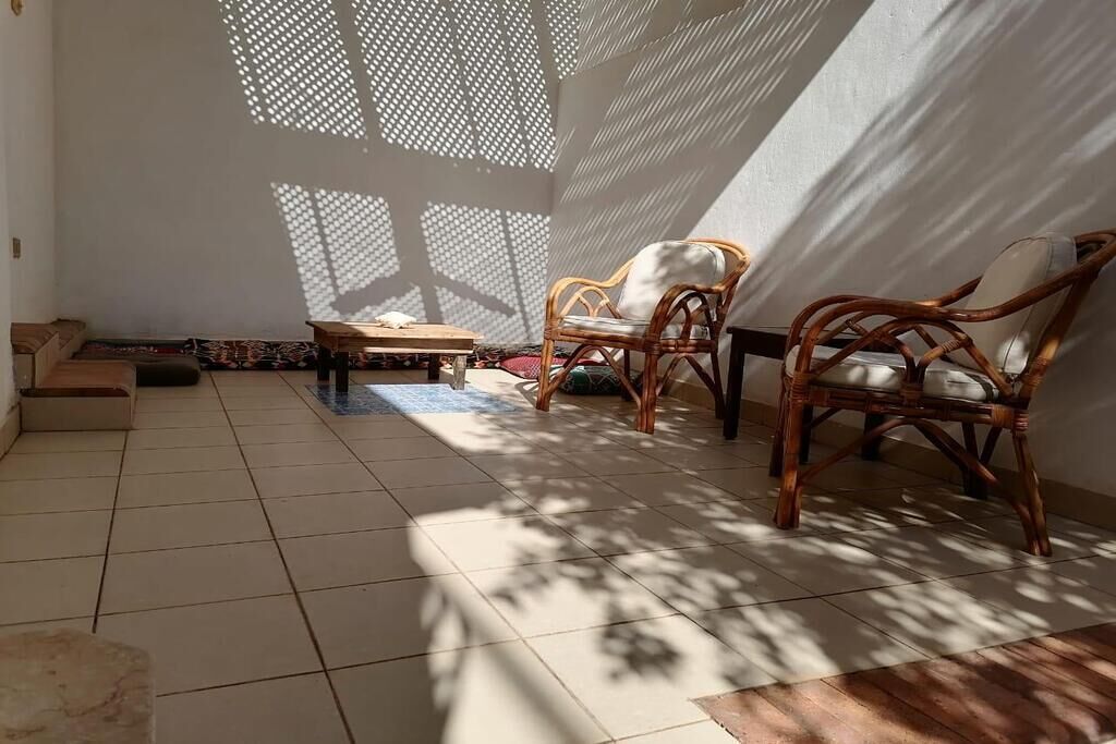 Une pièce dont le sol est recouvert de carreaux, avec deux fauteuils en osier, une petite table en bois et un tapis à motifs.