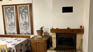 Una stanza accogliente con camino, un tavolo con tovaglia, un armadio in legno e una finestra con tende decorative.