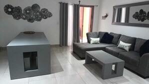 Una sala de estar moderna con un sofá seccional gris, una pequeña mesa de centro gris y una mesita auxiliar gris. Hay una pieza de arte decorativo sobre el sofá y una pequeña decoración de mariposa en la pared.