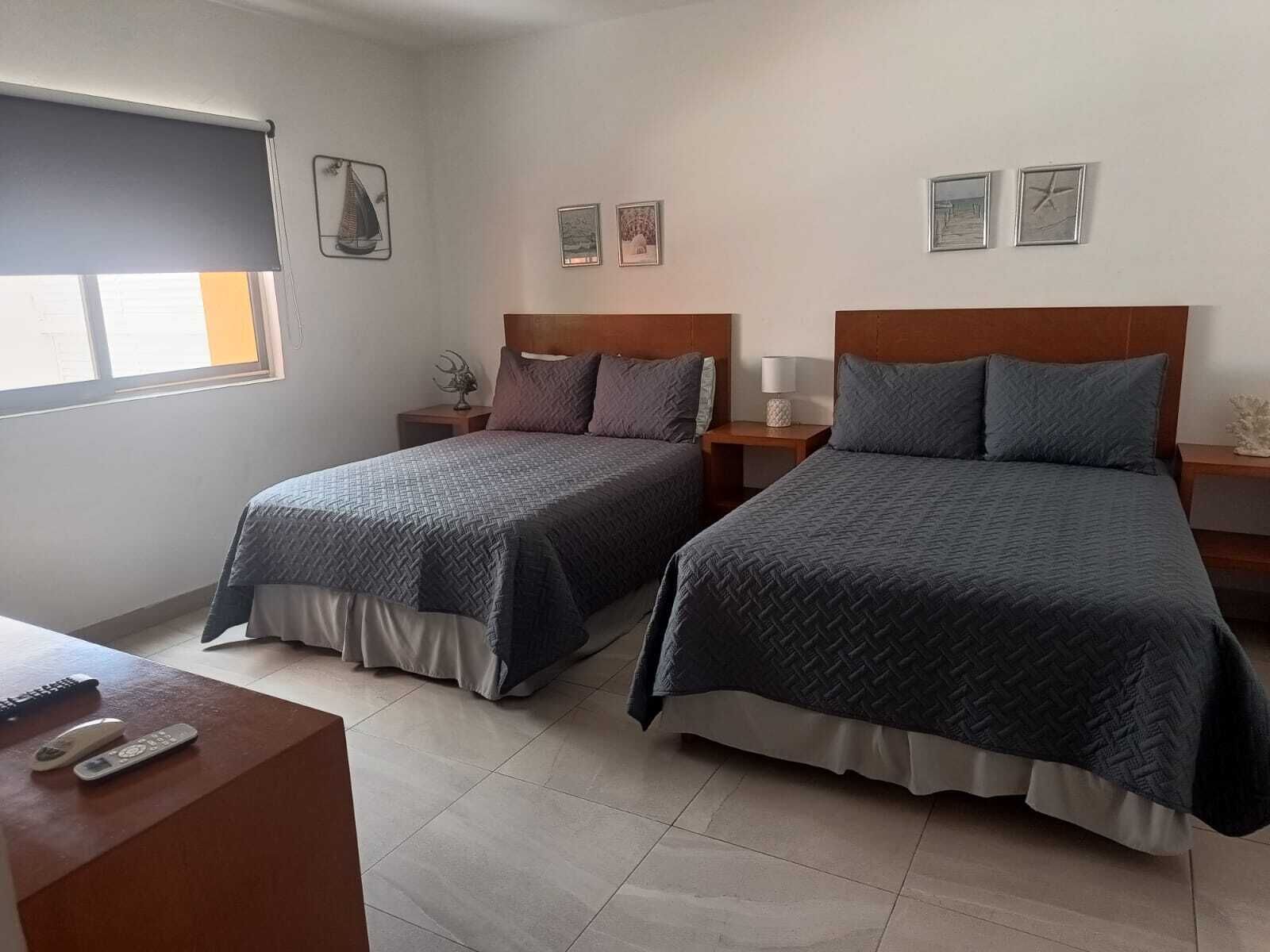 Una camera d'albergo con due letti, una scrivania e una finestra con tende.
