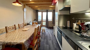 A cozy kitchen with wooden cabinets, a dining table with chairs, and a view to the outside. - Warm and cozy apartment, 250 m from the slopes, fully renovated, sleeps 6 (La Plagne Tarentaise)